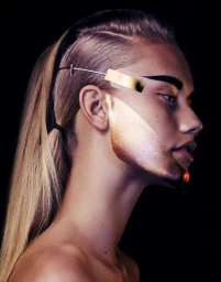 Close-up profile portrait of a woman with metallic gold makeup and a geometric gold bar accessory over her eyebrow.