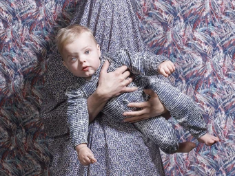 Baby in blue patterned romper held by adult against a vibrant blue and red patterned background