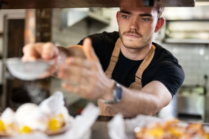 Chef dusting pastry with flour, in a kitchen. Food preparation scene with a baker at work creating treats in restaurant setting.