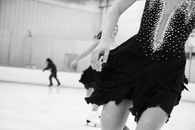 Two figure skaters in sparkling dresses performing on ice, with another person skating in the background, creating a dynamic winter scene.