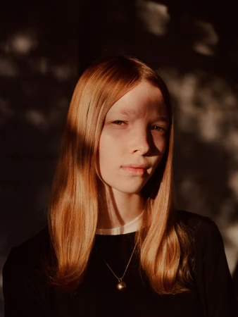 Portrait of a young woman with strawberry blonde hair in a black top, featuring soft, natural lighting and a minimalist aesthetic.