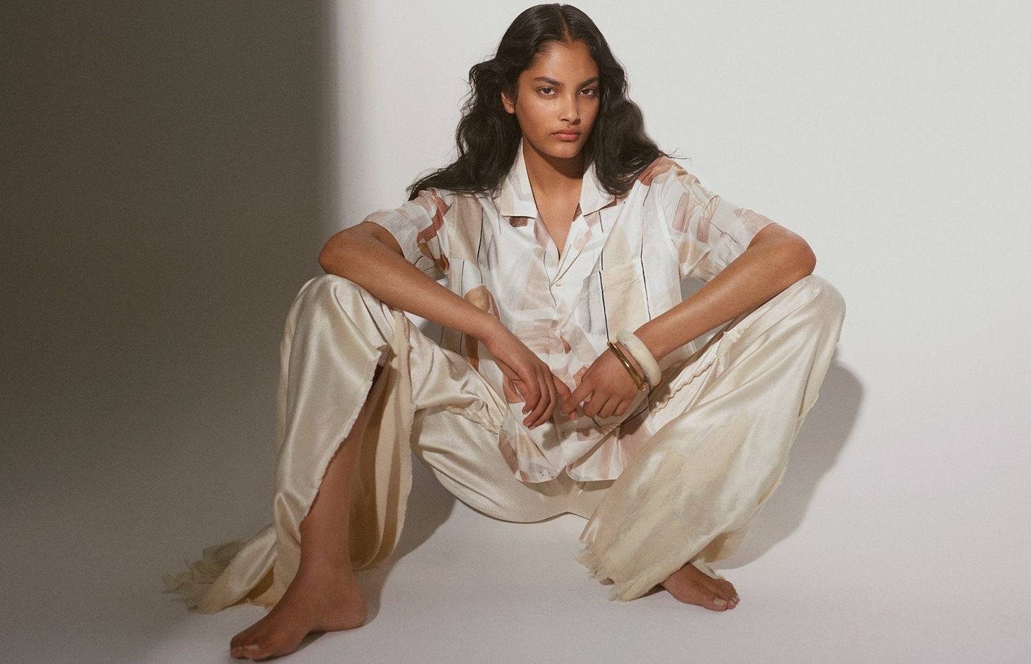 A person in patterned pajamas sits on the floor. The outfit is light-colored with subtle pattern details, posed against a white background.