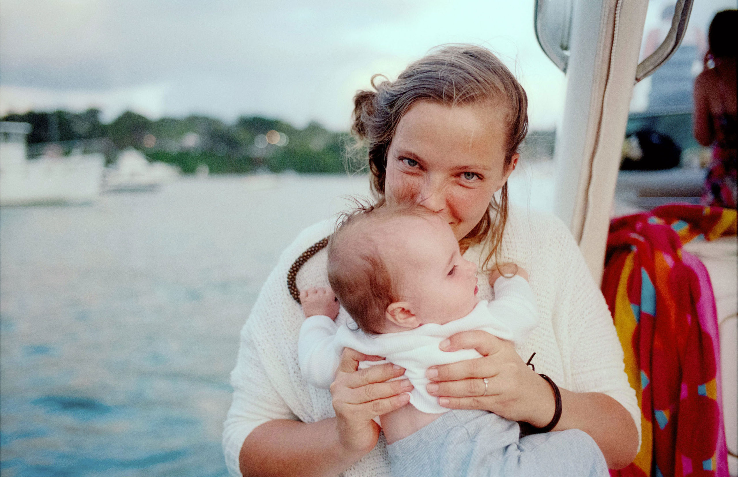 Woman holding a baby on a boat with an ocean backdrop, creating a tender and serene scene, with diffused lighting.