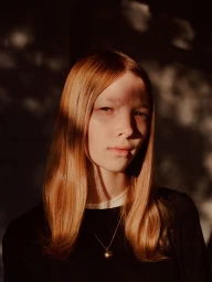 Portrait of a young red-haired woman wearing a black top and pendant necklace under dappled sunlight by Bec Lorrimer.