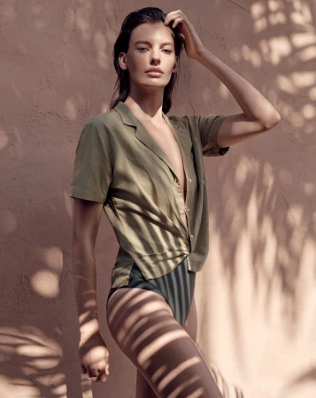 Model in olive green shirt and dark bottoms posing against a textured wall with leaf shadow patterns styled by Marina Afonina