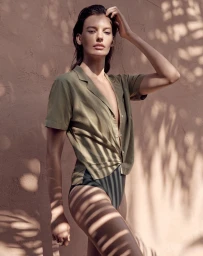 Model in olive green shirt and dark bottoms posing against a textured wall with leaf shadow patterns styled by Marina Afonina