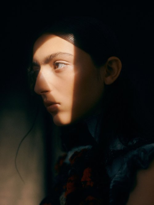 Portrait of an adult female with fair skin and dark hair, angled light stripe across the face, and wearing a dark floral top.