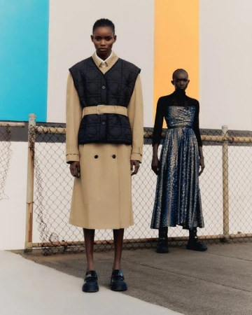 Two fashion models pose outdoors wearing tan trench coats and dresses against a striped backdrop. Street-style fashion editorial.