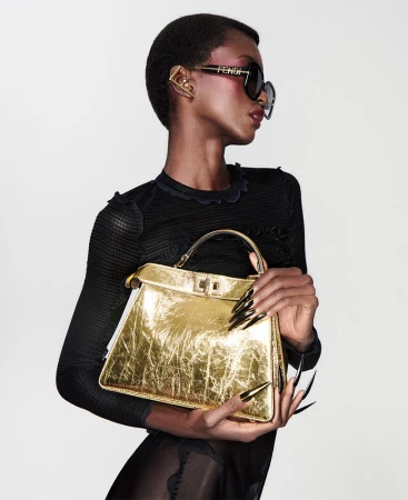 Fashion shot of a Black female model wearing sunglasses and holding a gold handbag, showcasing style and luxury in a studio setting.
