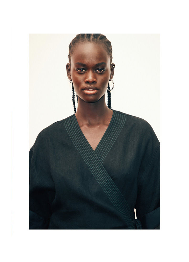 Portrait of a stylish young adult woman wearing a V-neck wrap top with braided hair against a white background in a studio shot.