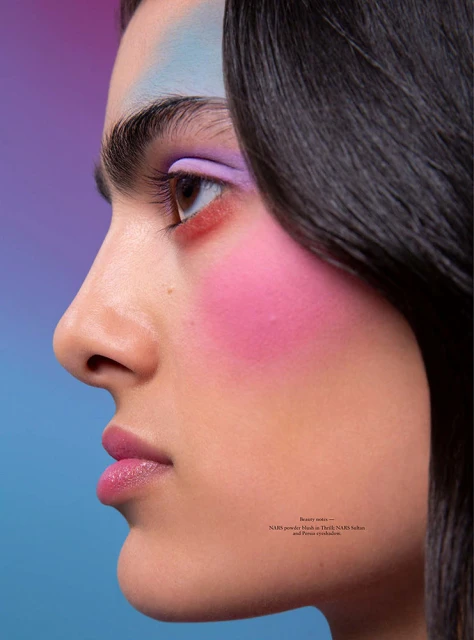 Beauty shot of a woman's face in profile with vivid makeup including pink blush, lavender eyeshadow, and light blue on her eyebrow.