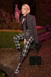 Blonde woman wearing a grey tweed coat and plaid trousers seated on a park bench at night