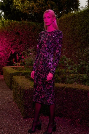 Model in sequined dress standing in a hedge garden under pink lighting photographed by Sebastian Kriete