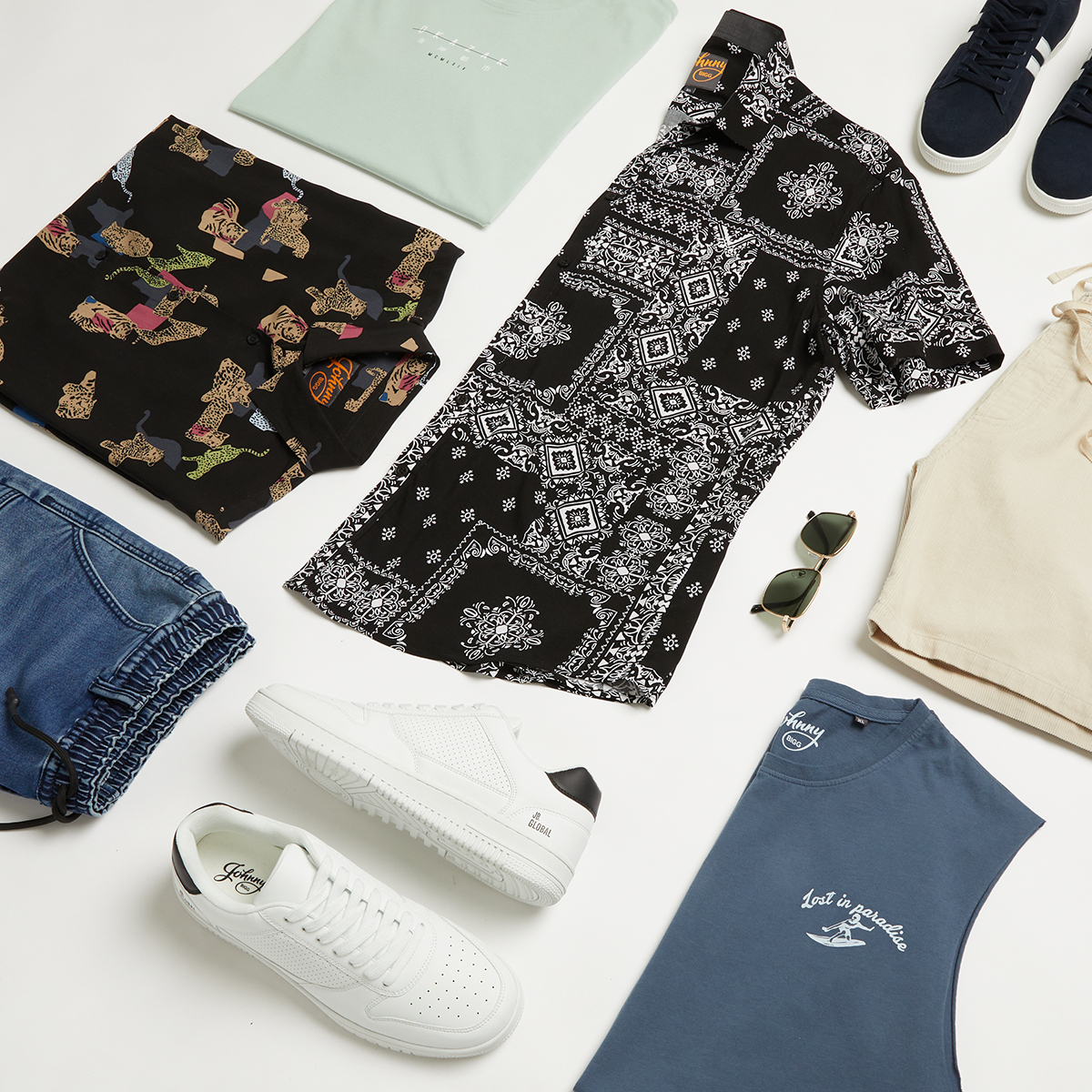 Flat lay of men's fashion apparel and accessories on a white background, including shirts, pants, shoes, and sunglasses, arranged for a stylish display.