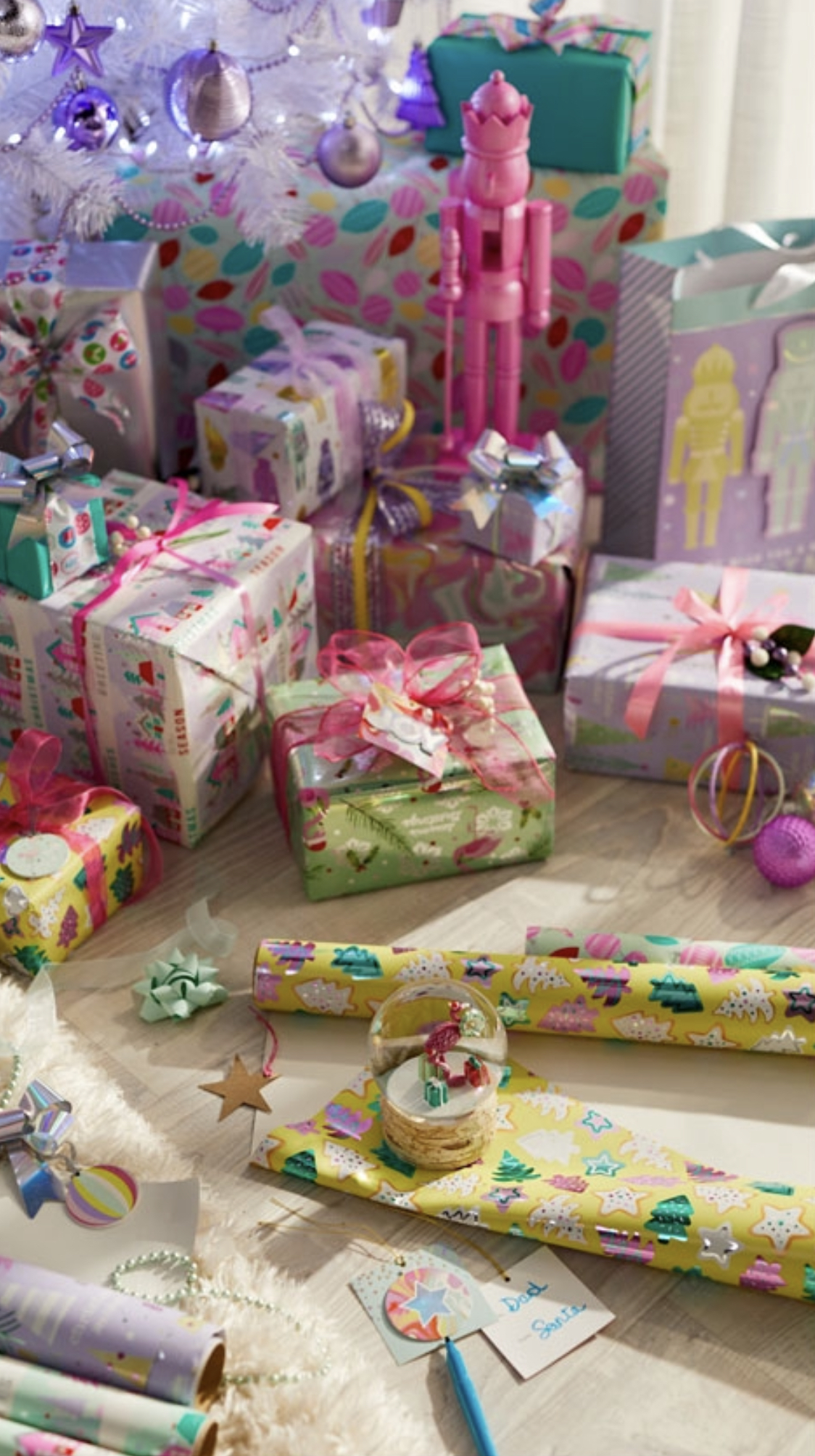 Festive holiday scene with wrapped presents, Christmas tree, wrapping paper, bows, and a snow globe creates a joyful ambiance.