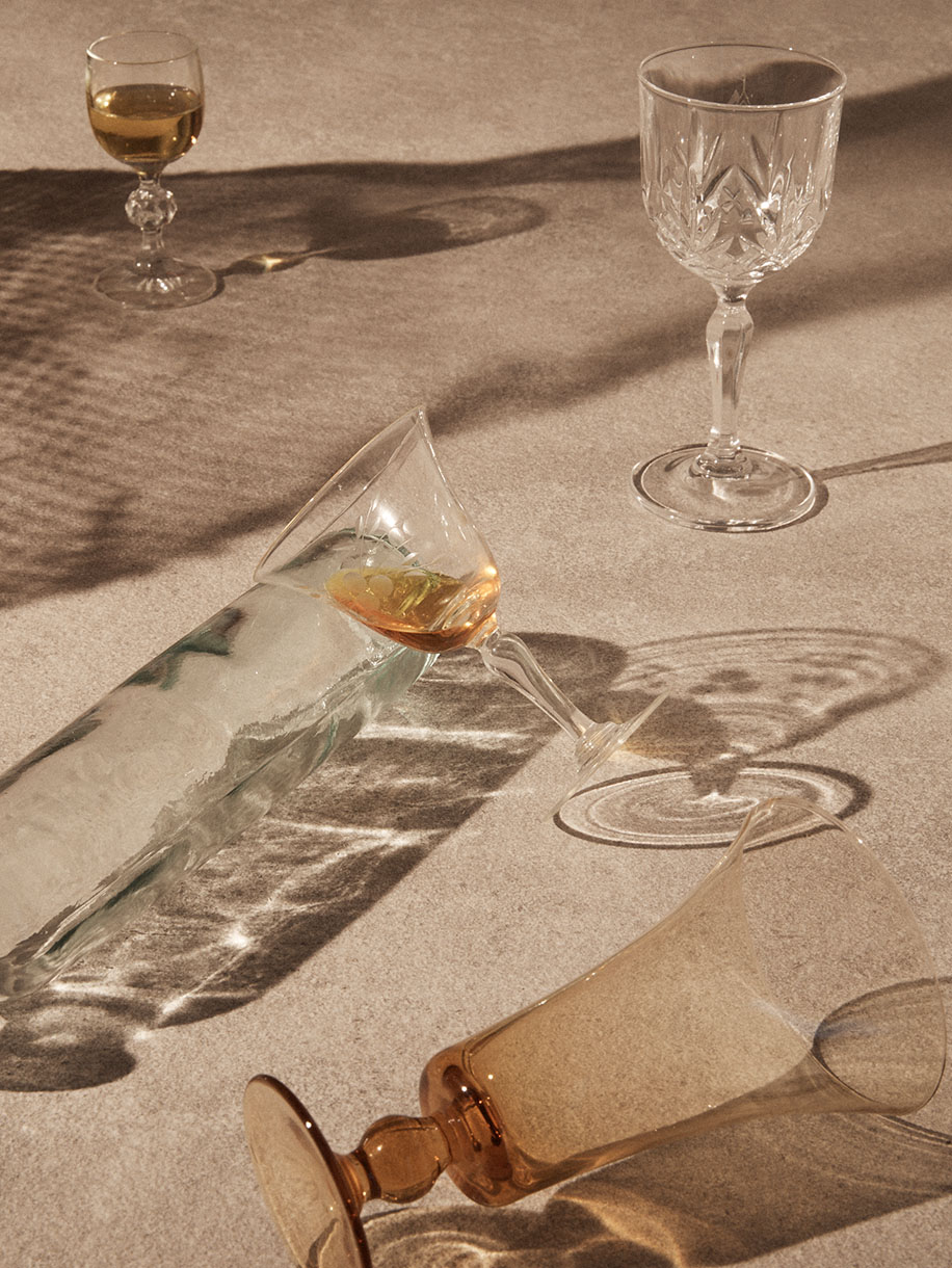 Elegant glassware arrangement featuring stemmed wine glasses, one tipped over, and refracted light patterns casting artistic shadows.
