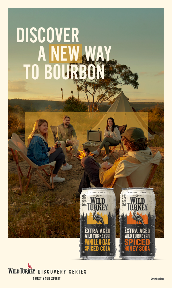 Wild Turkey Discovery Series ad showcases two cans against a backdrop of a campfire scene with four people enjoying an outdoor gathering.
