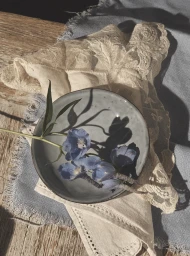 Overhead still life of blue flowers in a ceramic bowl resting on lace fabric and wooden surface