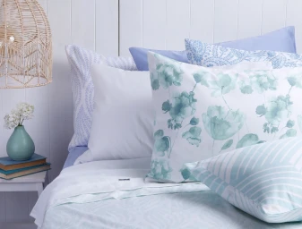 Close-up of a neatly made bed with layered patterned pillows and white sheets styled by Aurelie Tamin.