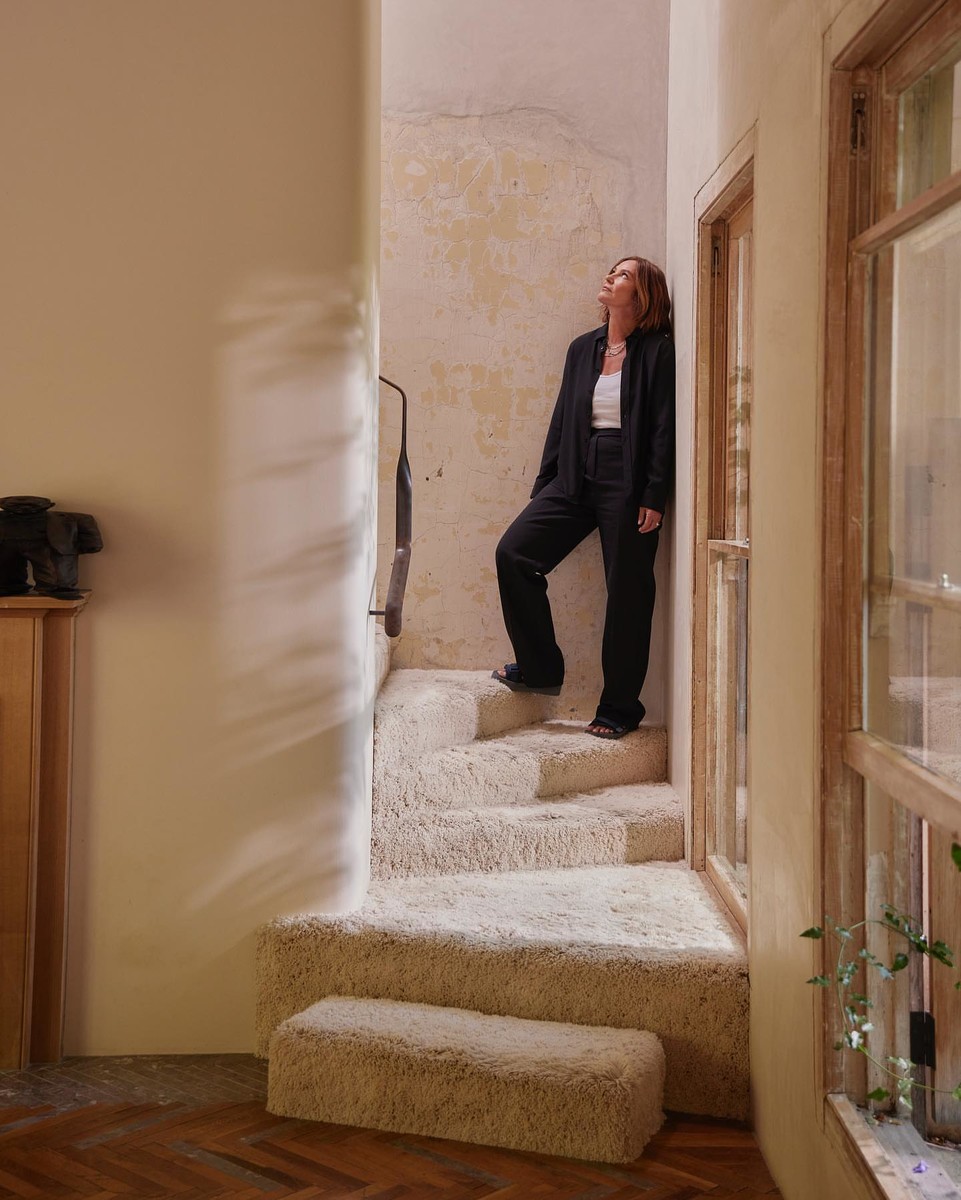 Woman in a black suit stands on carpeted stairs in an indoor setting, looking up towards a light source, side view.