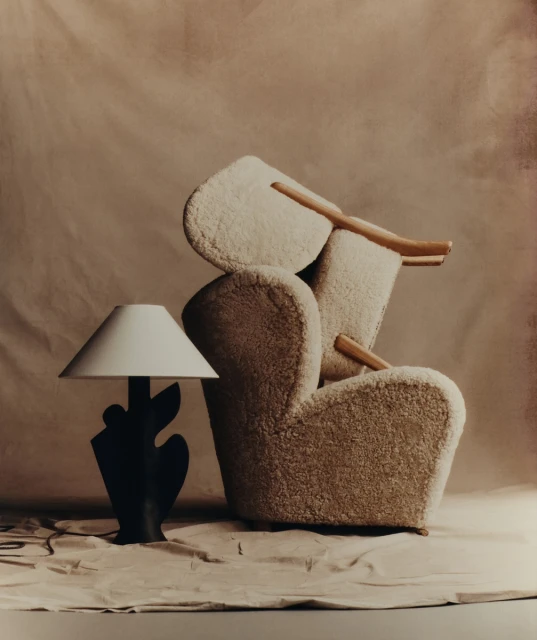 A photograph showcasing an elegant cream-colored armchair with wooden legs paired with a modern black lamp against a neutral backdrop.