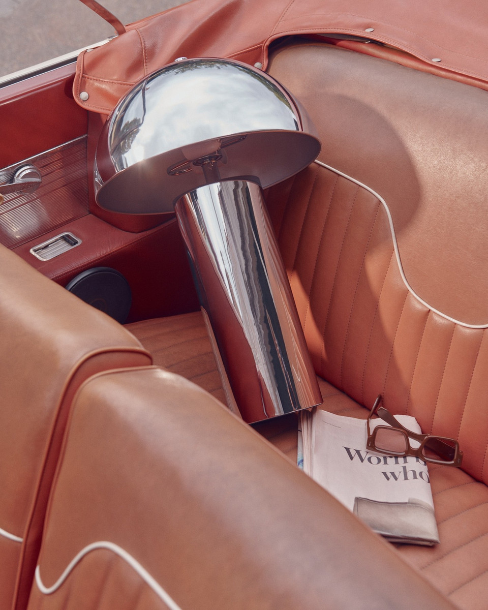 Still life of a silver mushroom lamp in a vintage car seat with a magazine, sunglasses, and orange leather interior, vintage automotive design.
