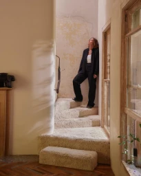 Woman in dark clothing leaning against a textured plaster wall on carpeted stairs designed by Joseph Gardner