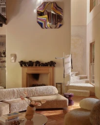 Modern interior living room styled by Joseph Gardner featuring a curved boucle sofa, wooden fireplace, and abstract wall art