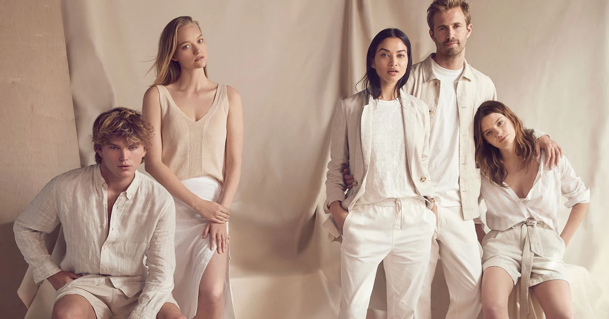 A group of five fashion models, two men and three women, in light beige and white linen clothing in a studio setting with a neutral backdrop.
