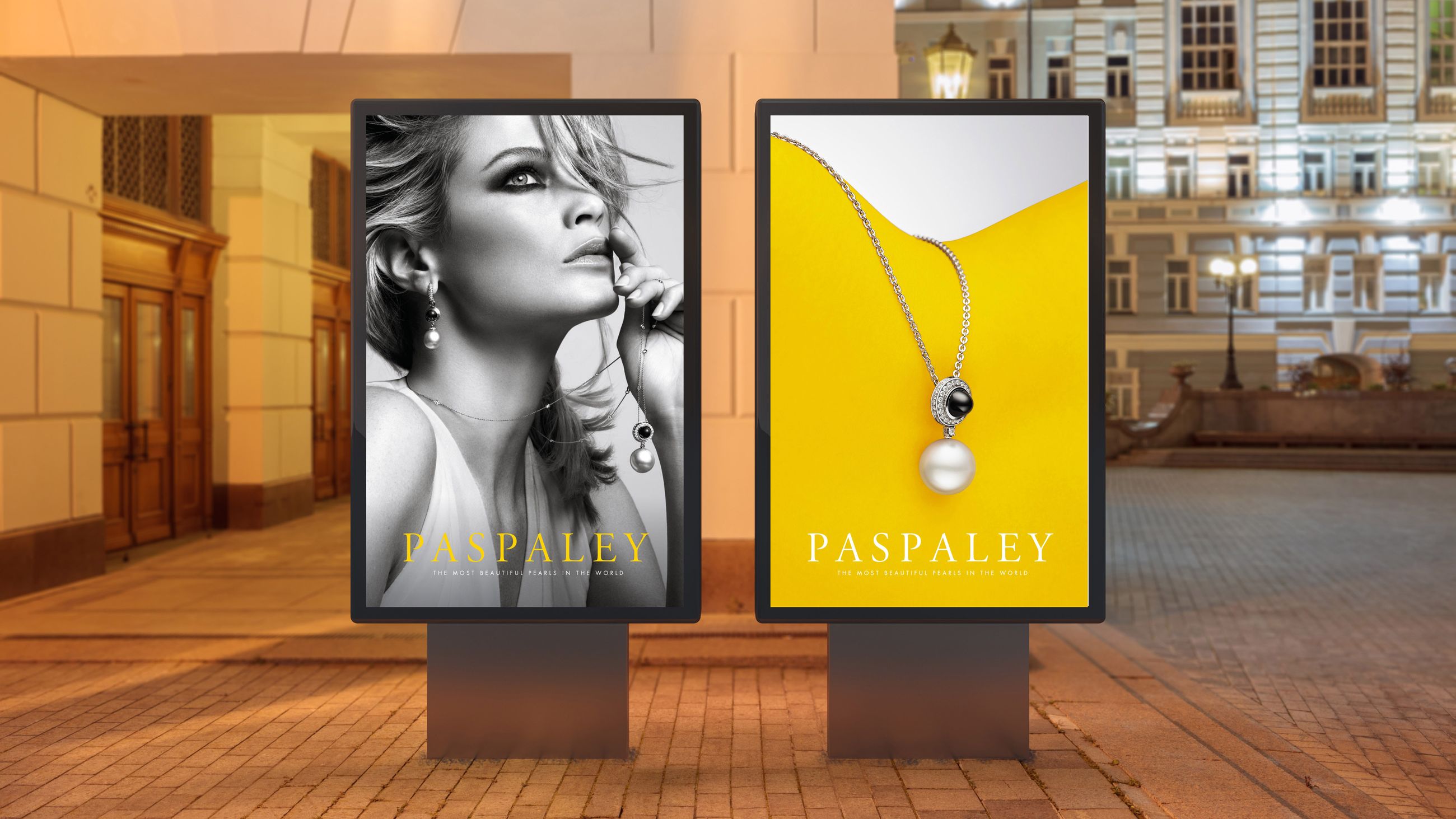 Two vertical advertising billboards displaying Paspaley pearl jewellery in a European city street at dusk.