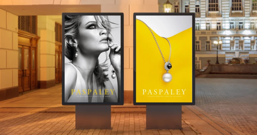 Two outdoor advertising displays showcase Paspaley jewelry: one with a woman wearing pearls, the other a pearl necklace on a yellow background.
