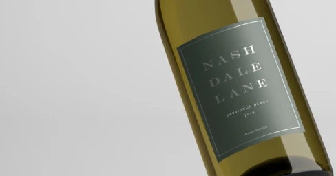 Close-up angled shot of a wine bottle featuring a dark green label with white lettering against a pale grey background.
