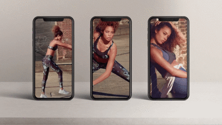 Three smartphones displaying fitness videos stand upright on a plain surface against a grey background.