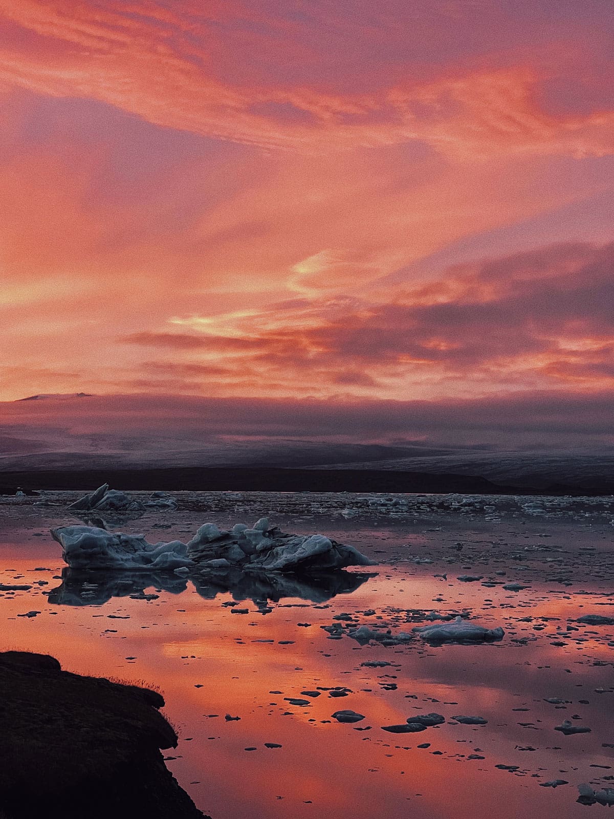 Tranquil sunset over a reflective body of water with icebergs and a hazy horizon in a cool and peaceful outdoor environment.