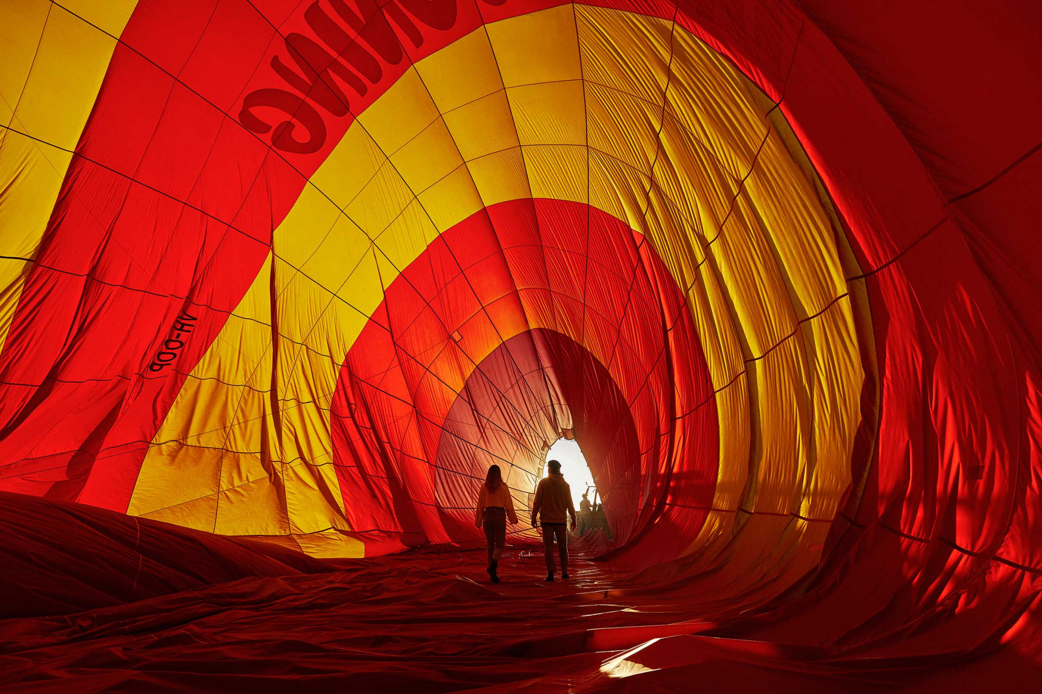 Inside a hot air balloon: Two people walk through red and yellow fabric, illuminated by natural light, creating a sense of adventure and travel.