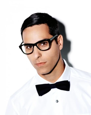 Portrait of a man wearing thick black framed glasses, a white dress shirt, and a black bow tie against a white background.
