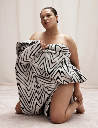 Model kneeling on a textured neutral floor while wrapped in a black and white zigzag patterned coat.
