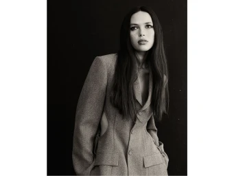 Monochrome portrait of a woman with long dark hair wearing a tailored cut-out blazer against a dark background