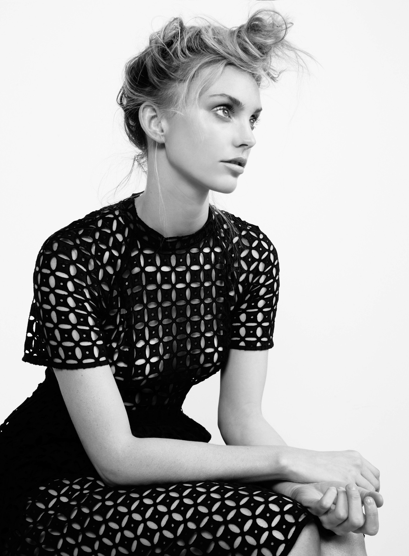 Black and white portrait of a blond adult female fashion model in a patterned black dress, seated against a plain white background.
