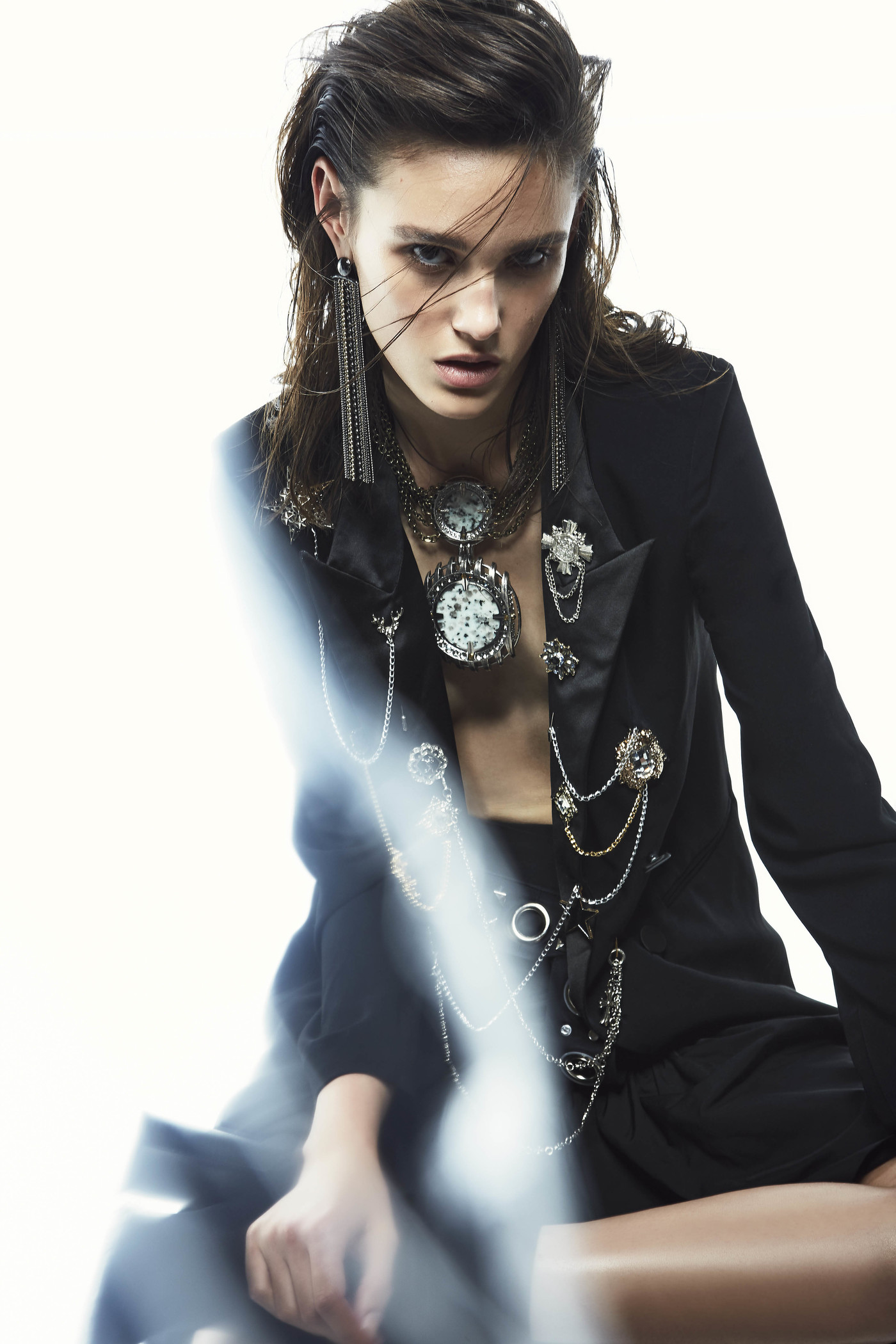 Woman in black blazer and statement jewelry poses in a fashion shot with bright studio lighting and a diffused lens flare effect.