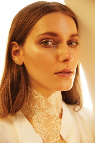 Close-up portrait of a fair-skinned woman with long brown hair and a lace collar, bathed in golden-toned lighting.