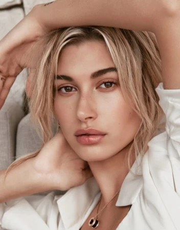 Close-up portrait of Hailey Bieber with blonde hair, neutral makeup, wearing a white shirt and necklace