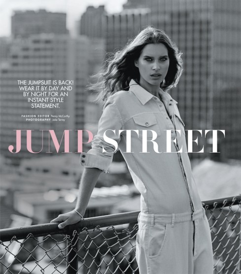 Model wearing a utility jumpsuit leaning on a rooftop railing against a city background