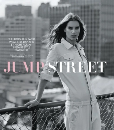 Model wearing a utility jumpsuit leaning on a rooftop railing against a city background
