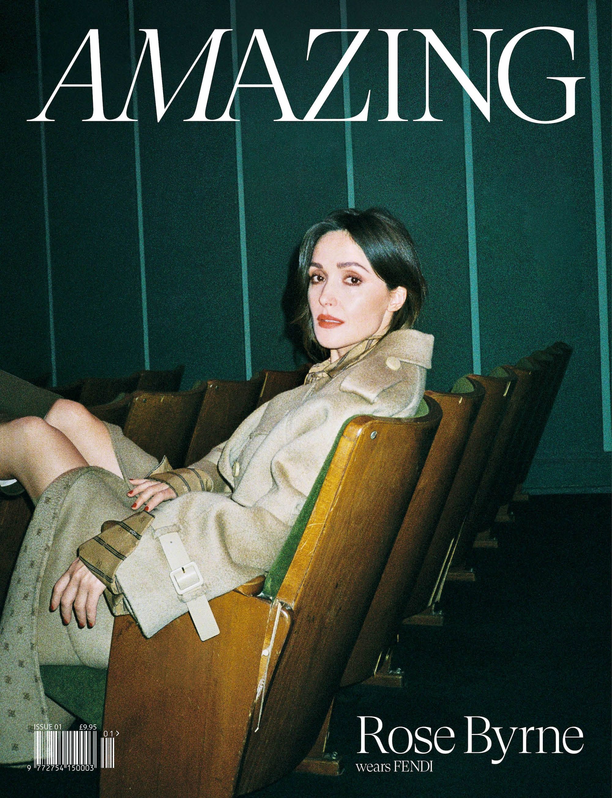 Rose Byrne on magazine cover in trench coat and patterned pants sitting in theatre chair. The magazine cover is titled, 'Amazing'.