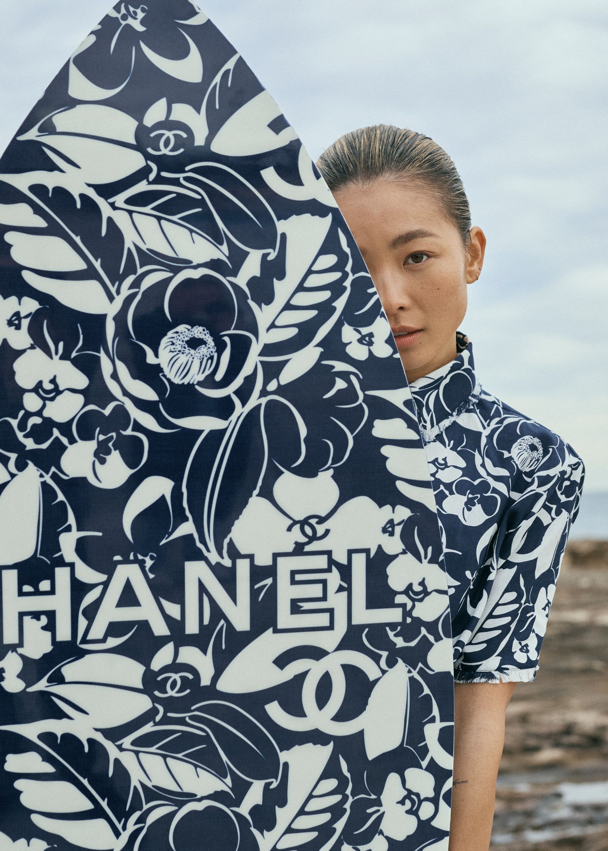 Woman posing with Chanel surfboard featuring floral pattern and the brand logo. The board and her top are the same design.