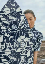 East Asian woman partially hiding behind a navy and white floral patterned surfboard by Chanel outdoors