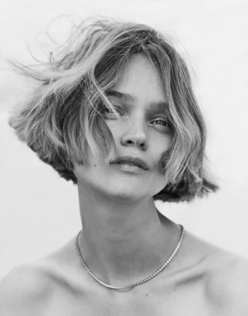 Close-up monochrome portrait of a woman with short messy hair and a thin chain necklace against a light background.