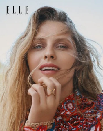 Close-up portrait of a blonde woman with hand near face wearing a colorful patterned top in an outdoor setting for Elle Australia.