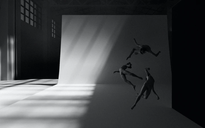 Monochrome image of three figures suspended in motion against a large curved white studio wall with dramatic diagonal light beams.